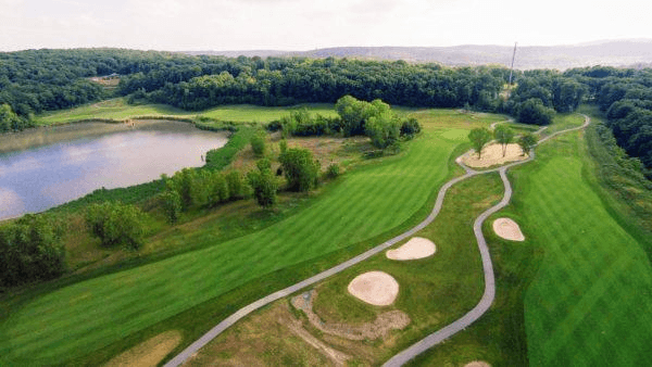 Aerial view of a lush golf course with sand traps and a pond surrounded by trees.