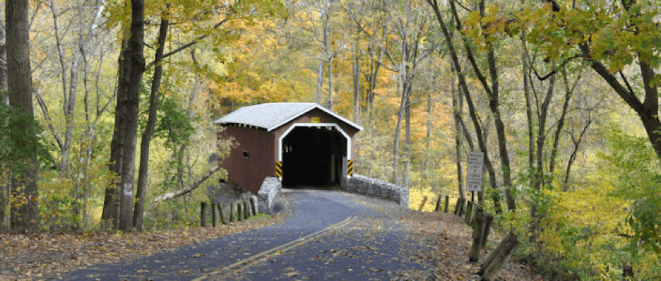 A covered bridge framed by colorful autumn foliage along a quiet road.