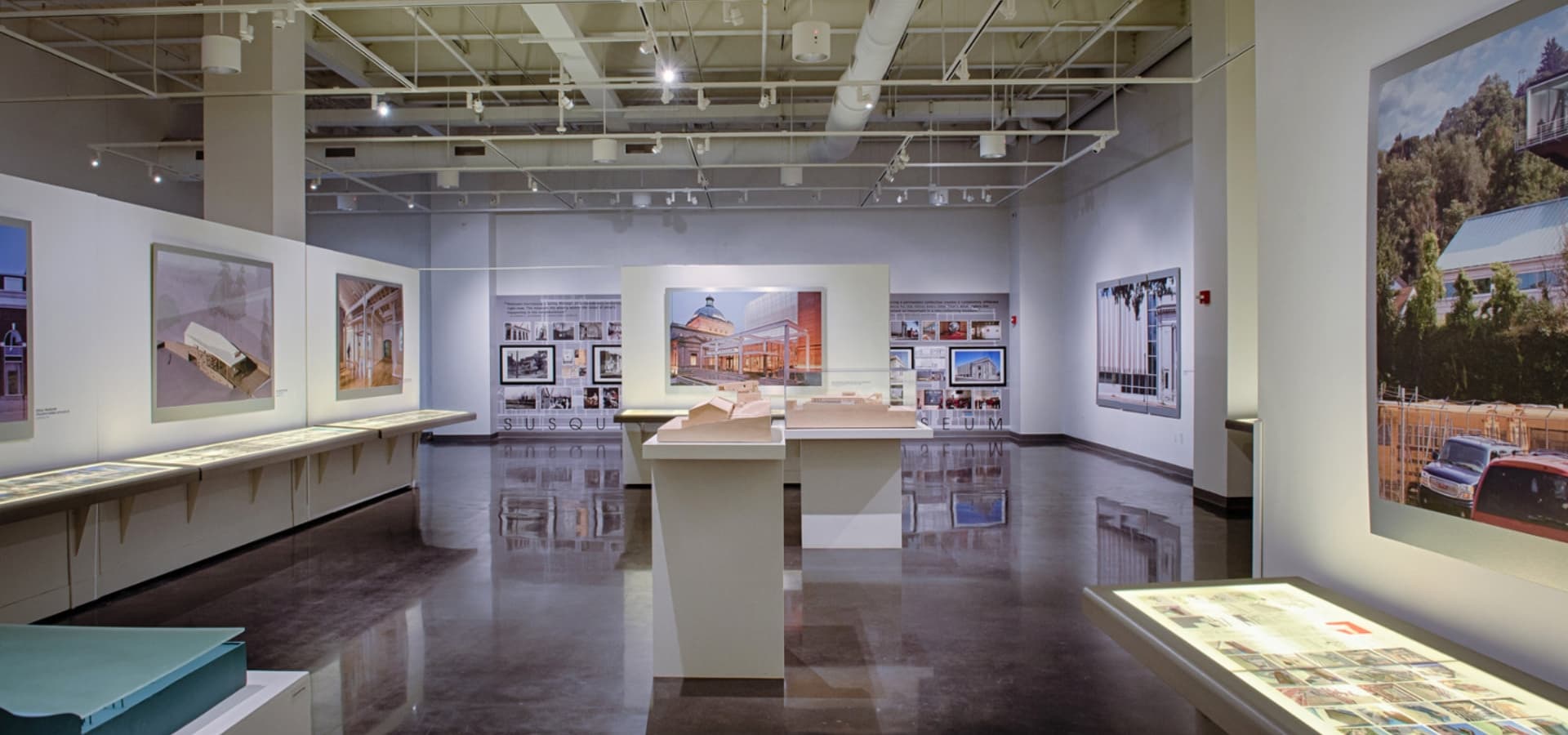 An art gallery featuring large photographs and models displayed on modern tables.