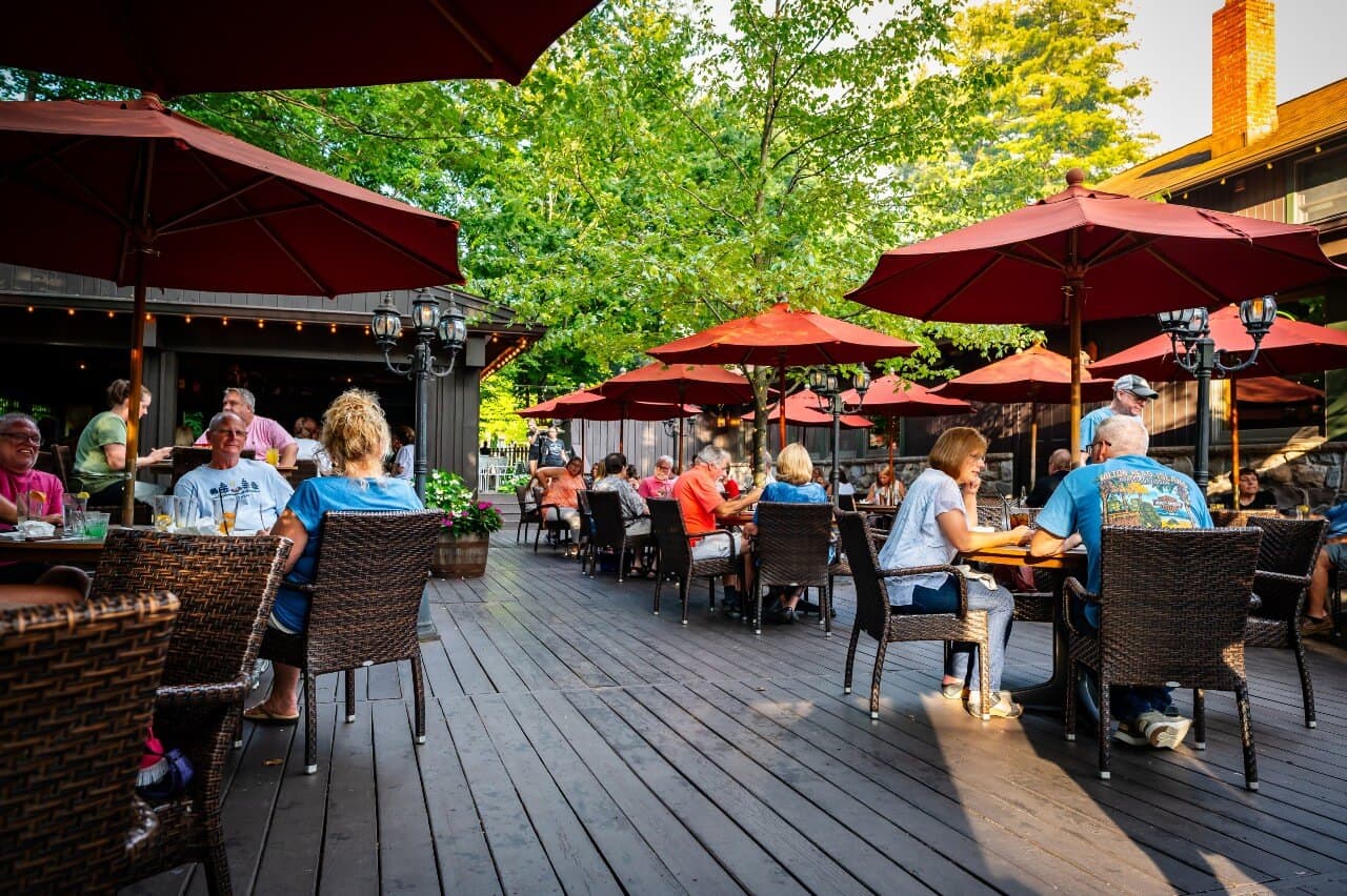 A bustling outdoor restaurant patio filled with diners under red umbrellas.