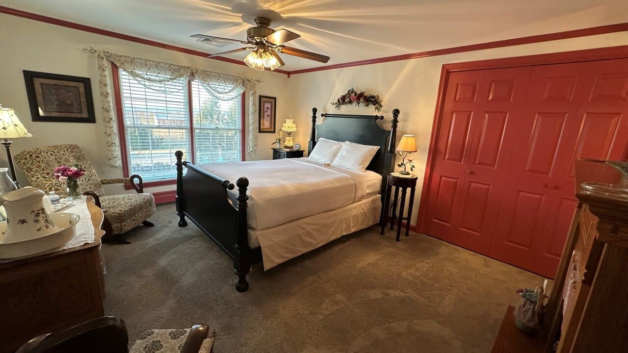 Cozy bedroom featuring a black four-poster bed, a vintage armchair, and red accents.
