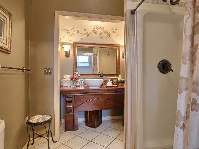 A well-decorated bathroom featuring a wooden vanity, mirror, and shower.