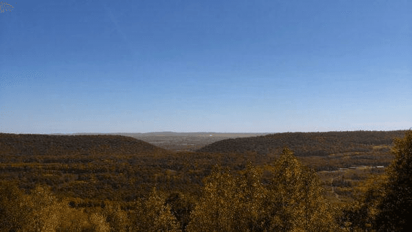 A panoramic view of rolling hills adorned with autumn foliage under a clear blue sky.