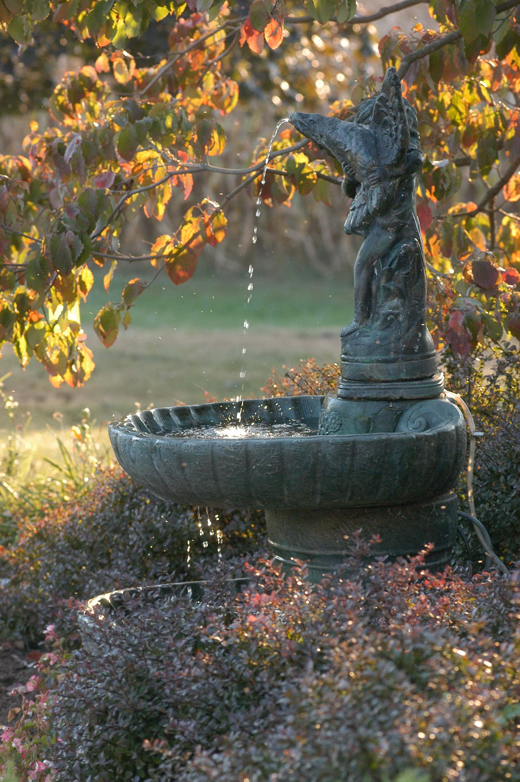 A decorative garden fountain with water flowing from a statue, surrounded by colorful foliage.