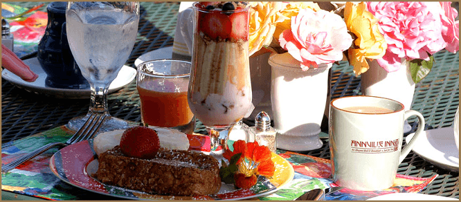 A colorful breakfast table featuring French toast, a parfait, juice, and coffee, surrounded by floral decor.
