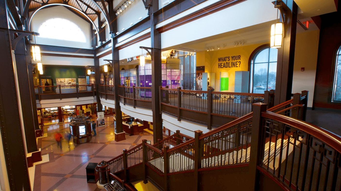 An interior view of a modern multi-level space featuring a staircase, large windows, and colorful exhibit areas.