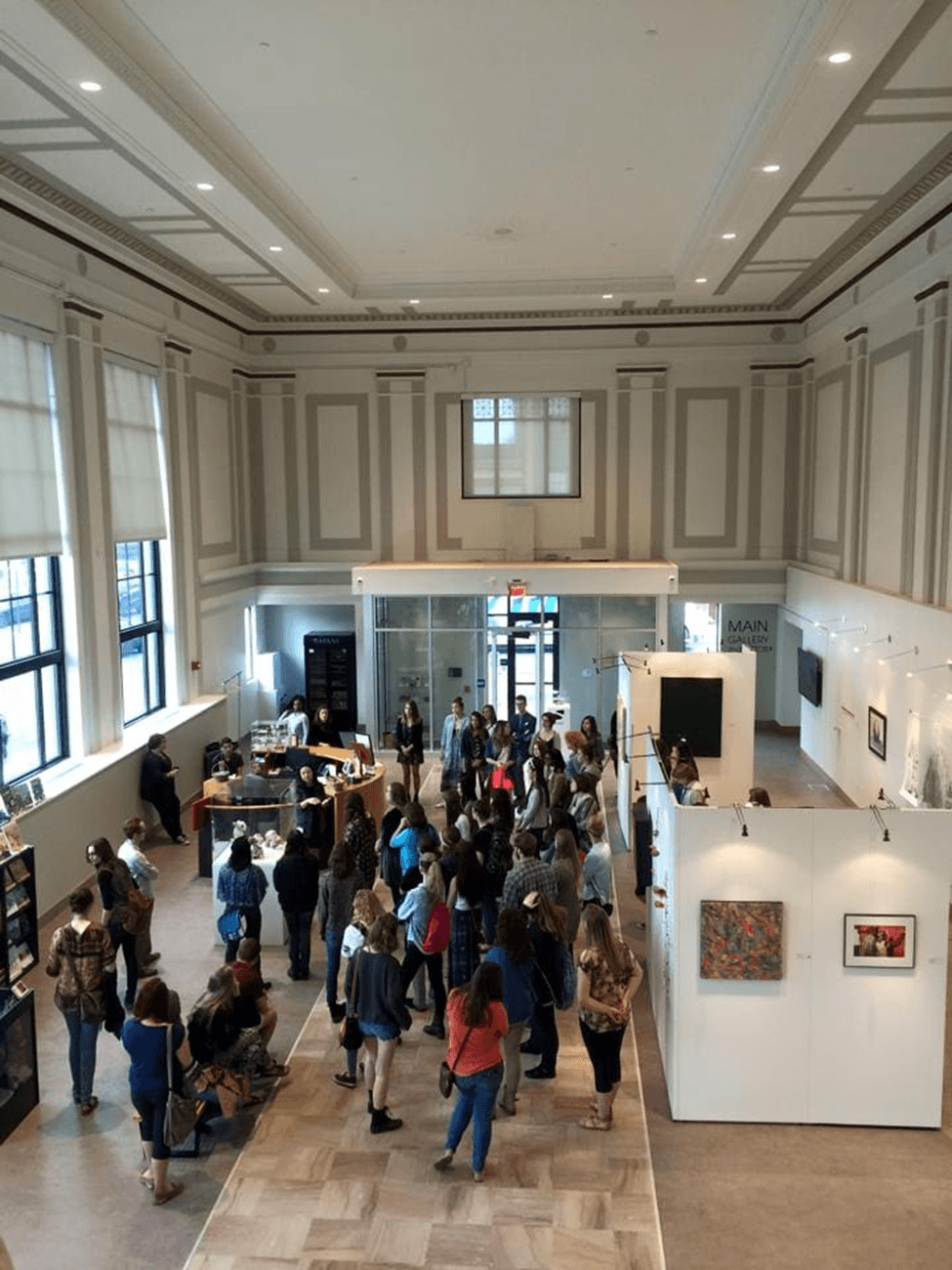 A large group of people gathers in an art gallery with white walls and exhibits.