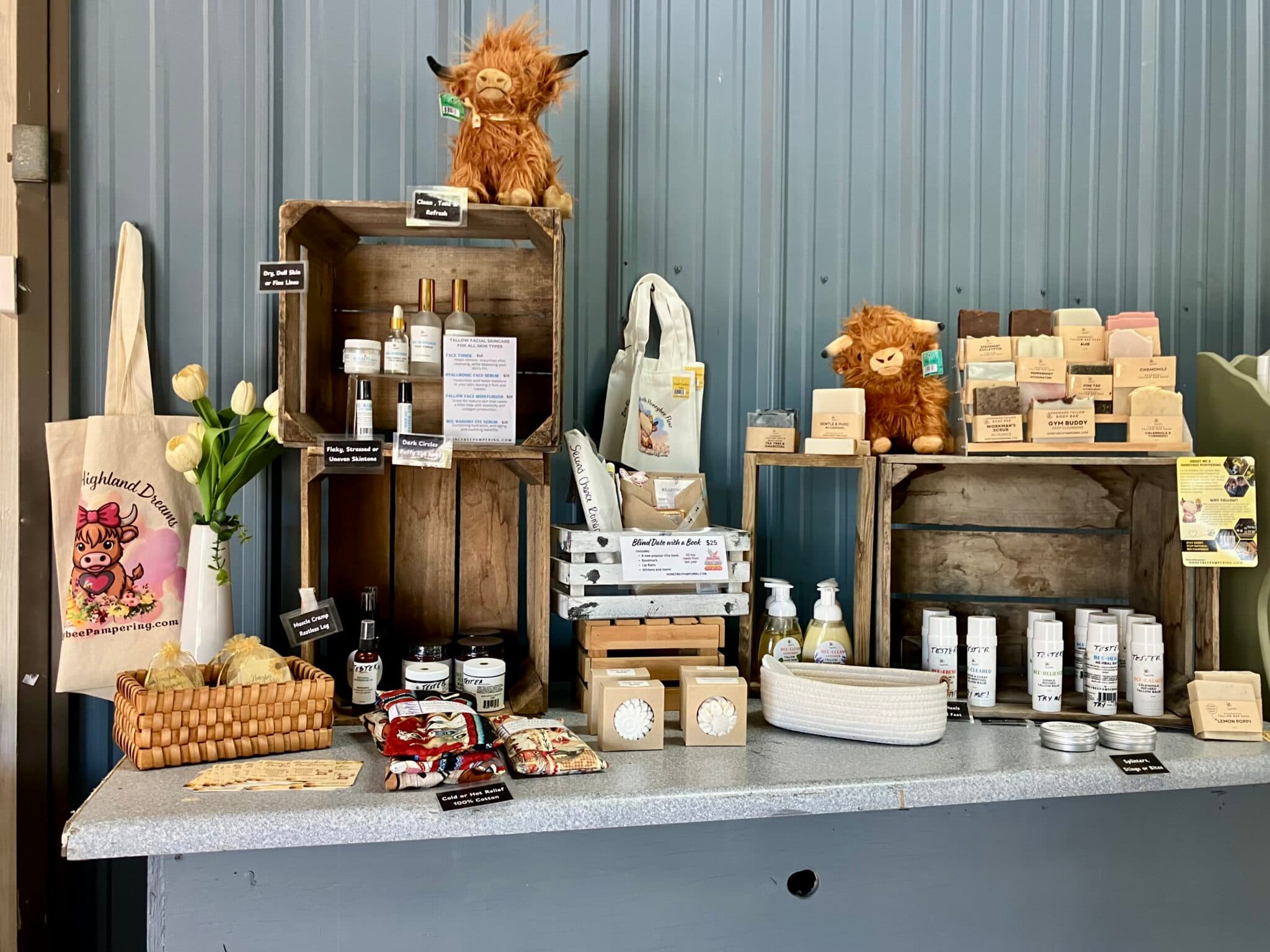 A display of handmade products including soaps, skincare items, and decorative plush toys, arranged on wooden shelves and a table.