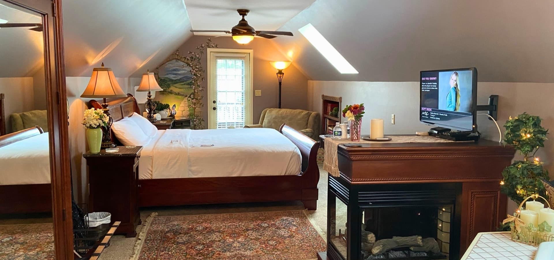 Cozy attic bedroom featuring a queen bed, TV, and a decorative fireplace.
