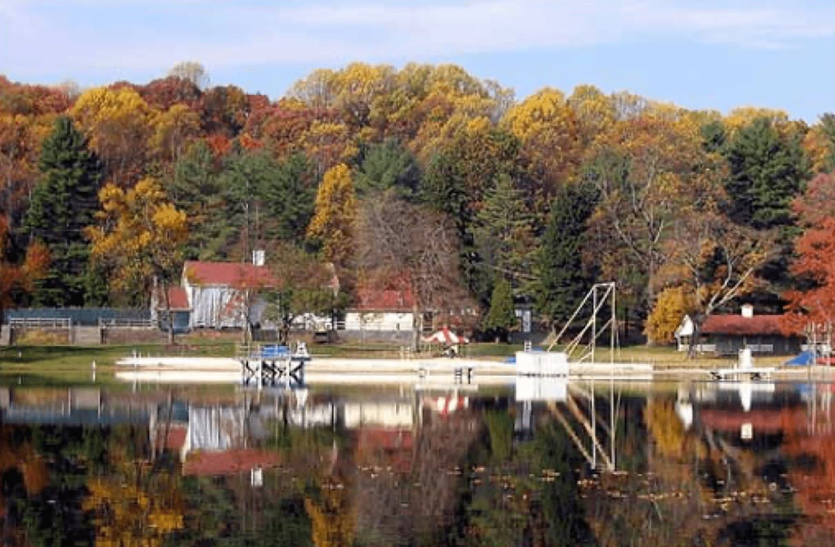 Scenic lake surrounded by colorful autumn foliage and reflecting a quaint building and diving platform.