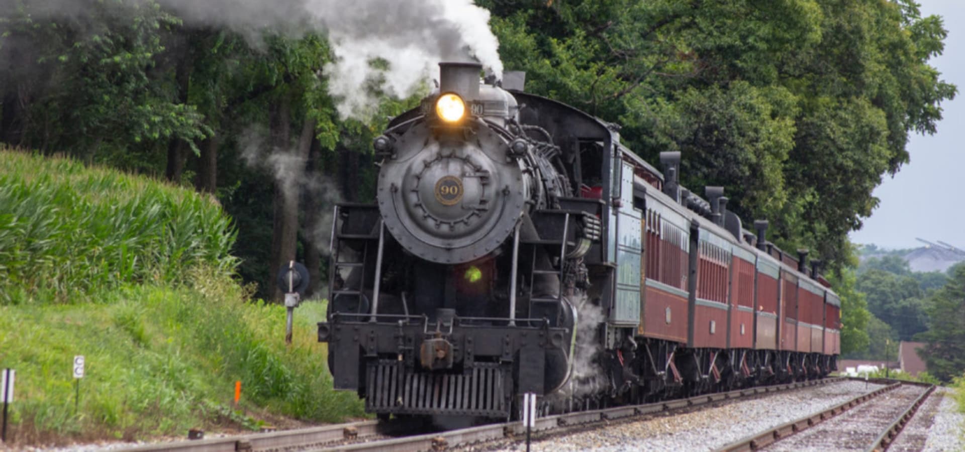 A vintage steam locomotive is chugging along a track surrounded by greenery.