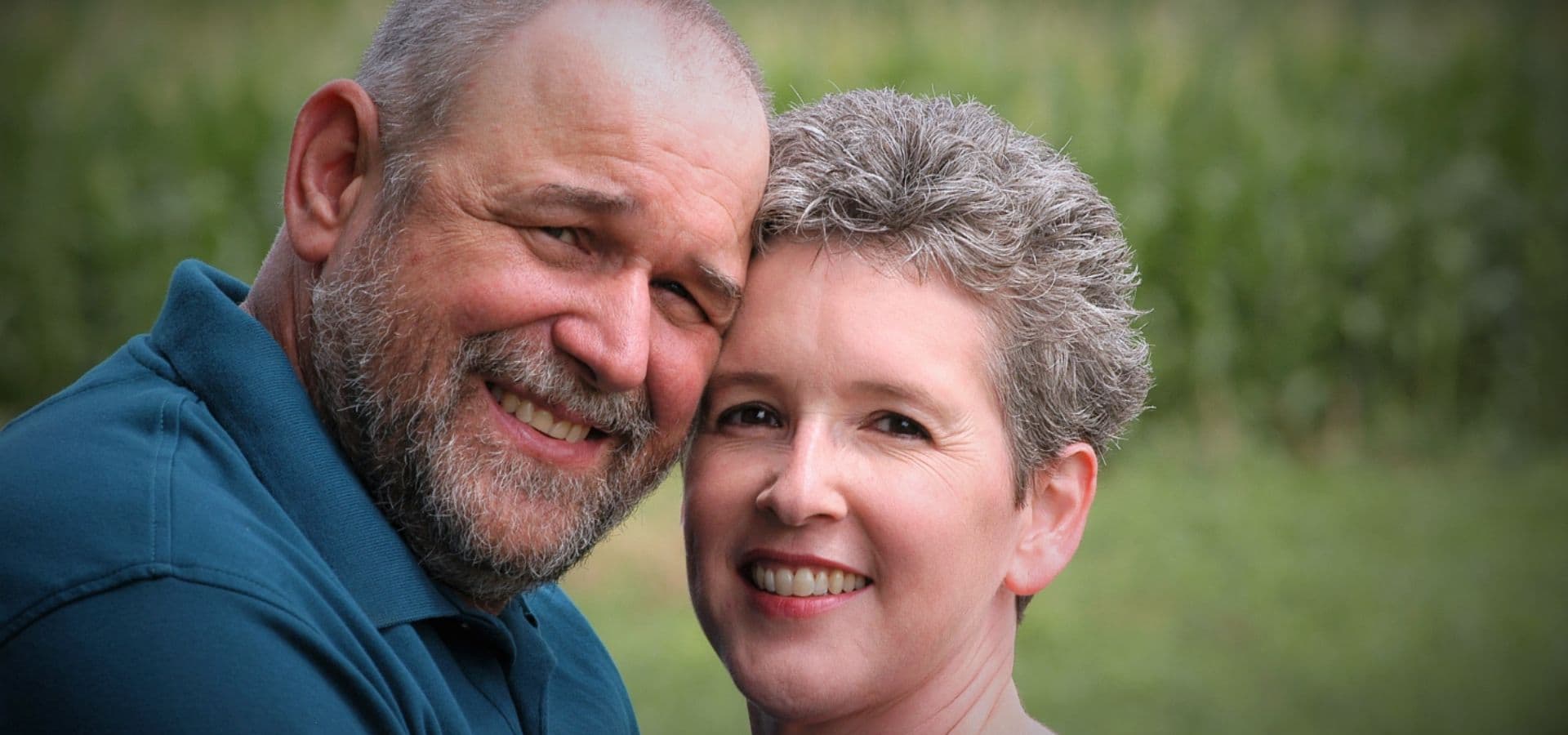 A happy couple smiles closely together outdoors.