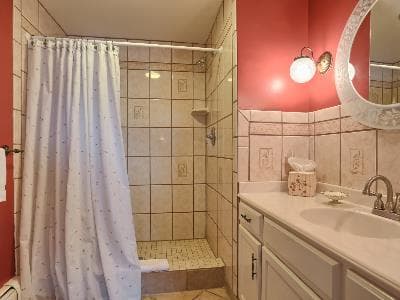 A bathroom featuring a tiled shower with a white curtain, a sink, and red walls.