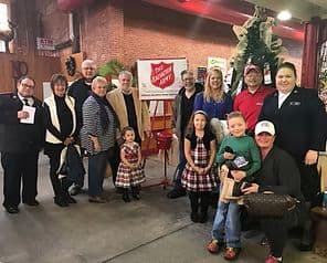 A group of diverse volunteers poses together in front of a Salvation Army donation kettle during a festive event.