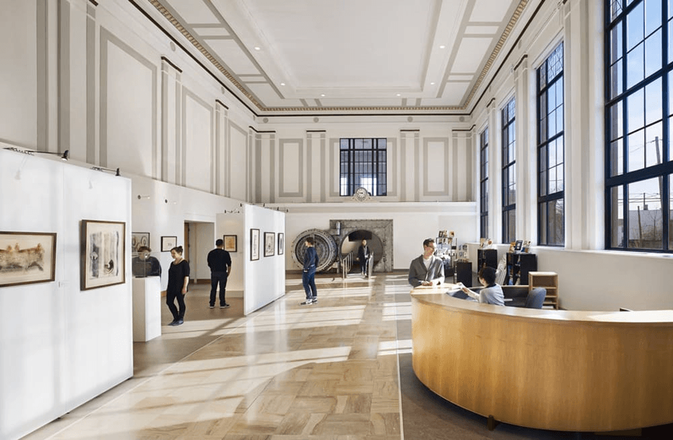 Interior of an art gallery with visitors exploring exhibits and a reception desk.