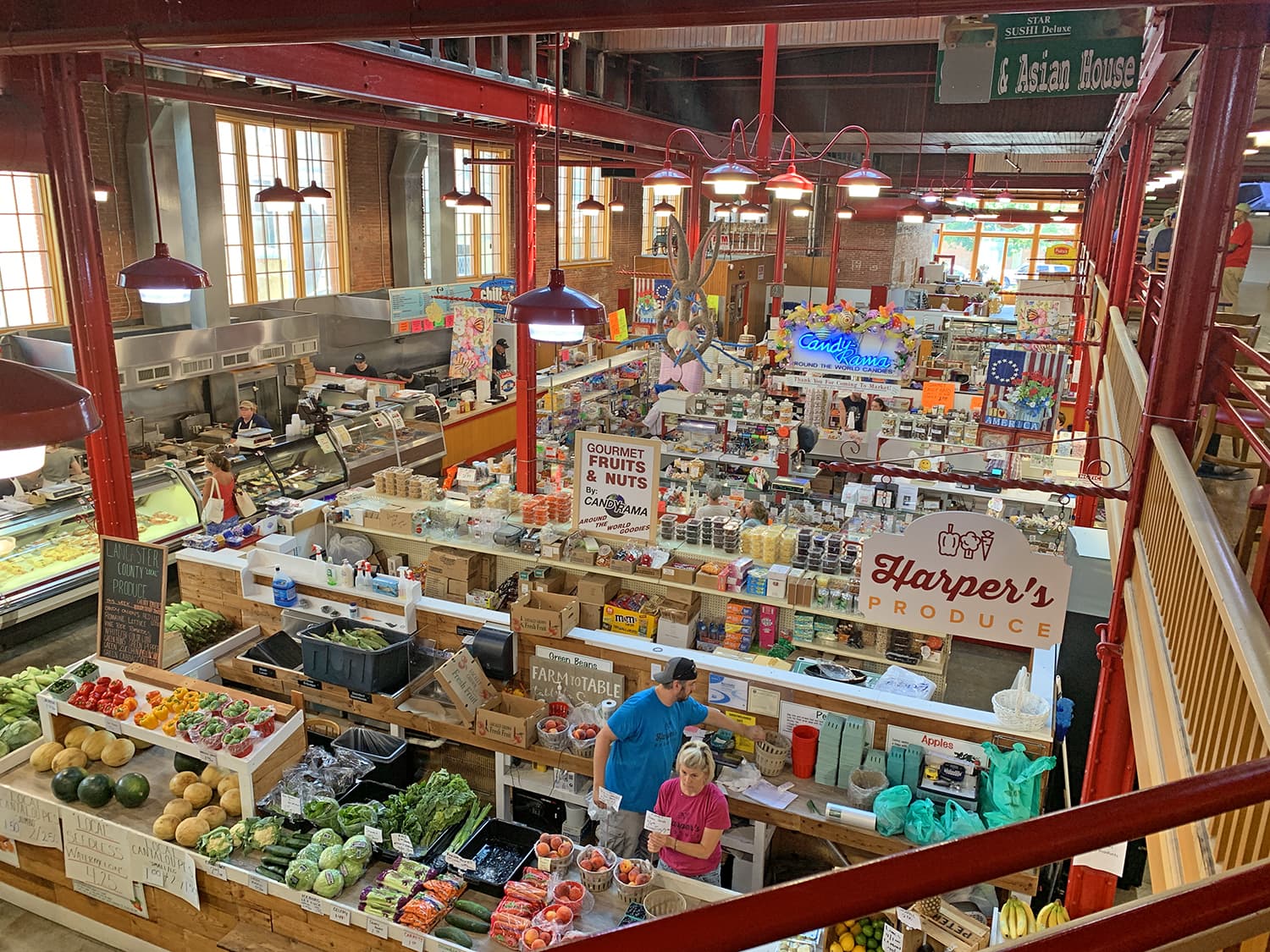 A vibrant marketplace filled with fresh produce, various food stalls, and shoppers browsing among colorful displays.