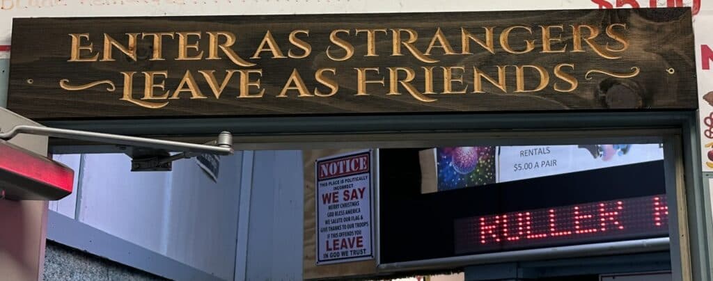 A wooden sign above an entrance reads, "Enter as strangers, leave as friends."