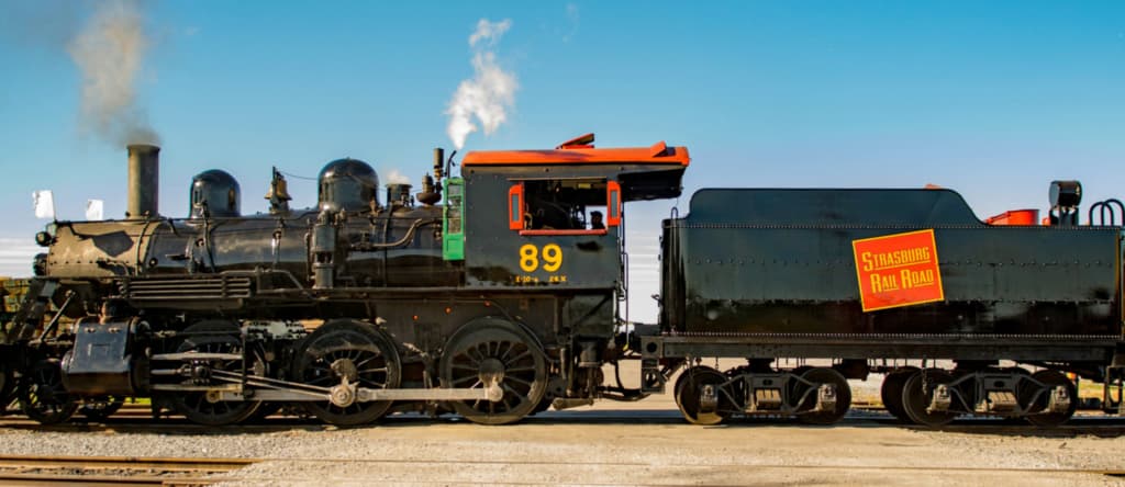 A vintage steam locomotive numbered 89, with smoke rising, parked beside its coal tender.