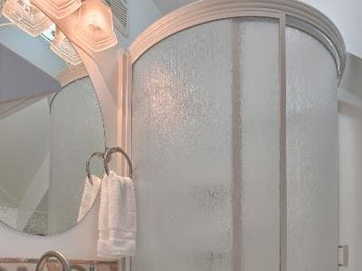 A bathroom featuring a frosted glass shower, circular mirror, and white towels.