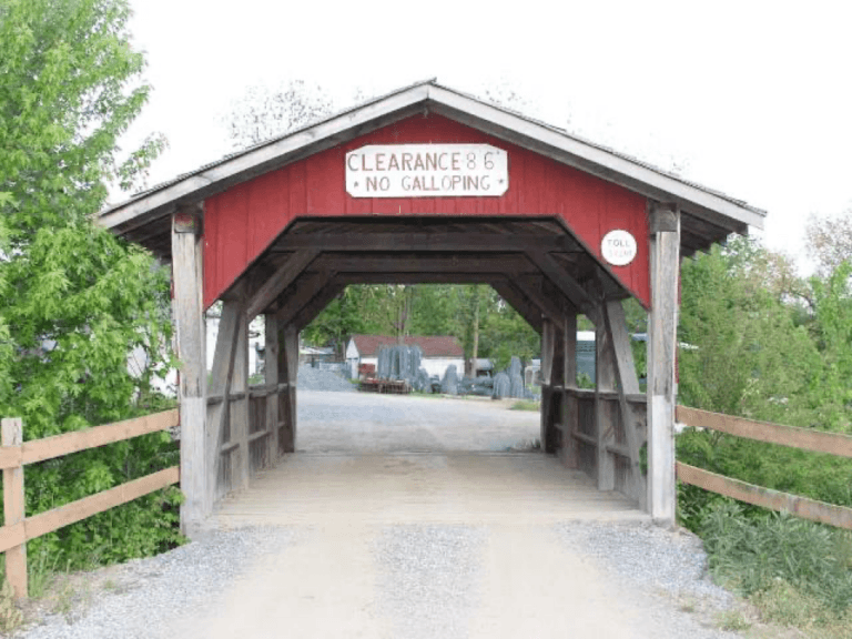 A wooden covered bridge with a sign indicating a height clearance of 8 feet 6 inches and a warning against galloping.