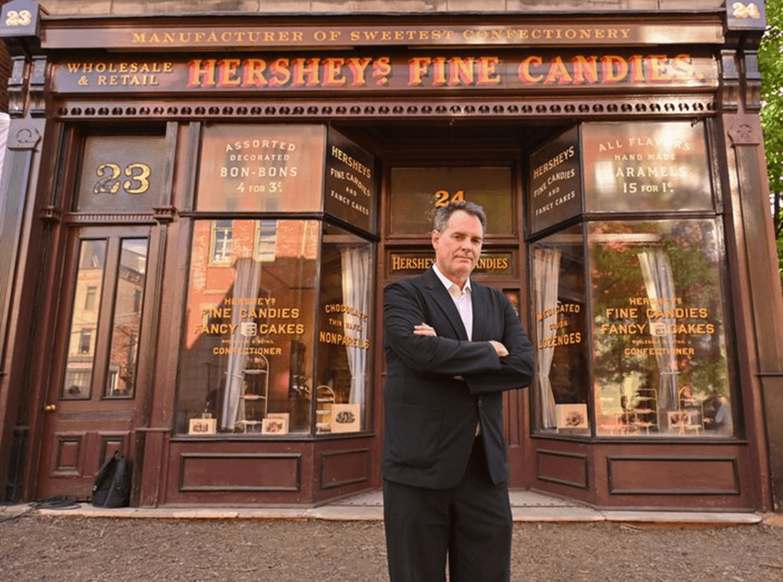 A man stands confidently in front of the vintage storefront of Hershey's Fine Candies.