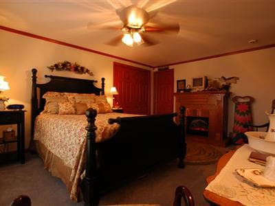 Cozy bedroom with a floral bedspread, a ceiling fan, and a fireplace.