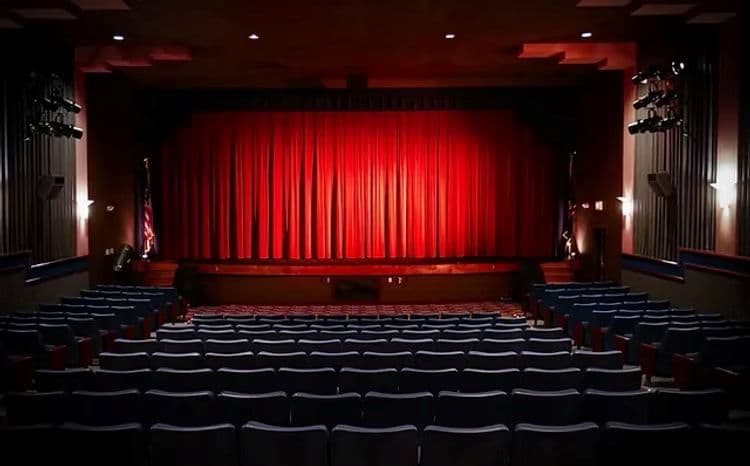 A dimly lit theater with a red curtain and empty seating.