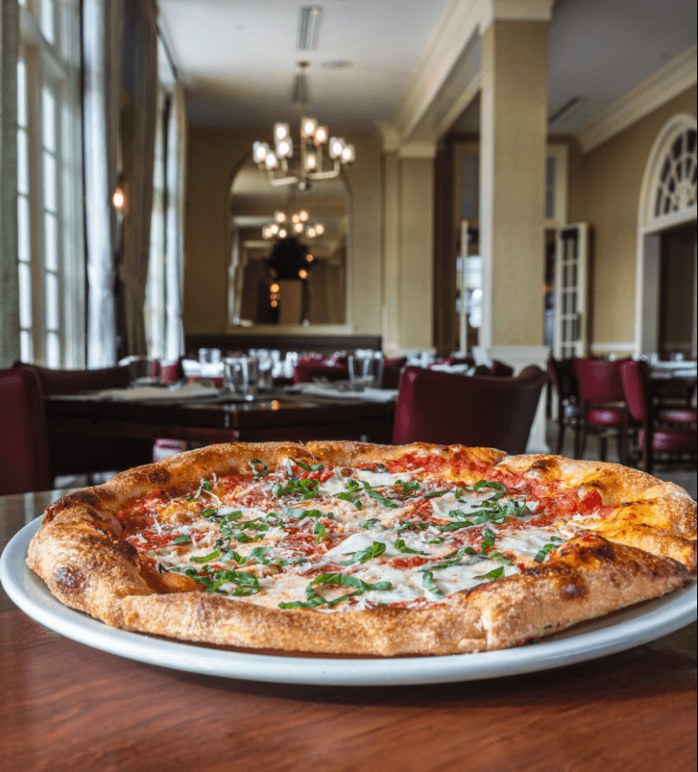 A freshly baked pizza topped with mozzarella and basil sits on a table in an elegant restaurant.