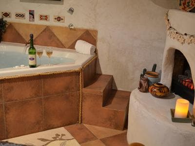 A cozy bathroom featuring a jetted tub with wine and glasses, decorative pottery, and warm lighting.
