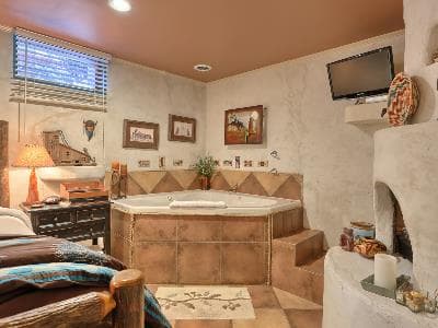 A cozy bathroom featuring a large jetted tub, a bed, a decorative fireplace, and framed artwork on the walls.