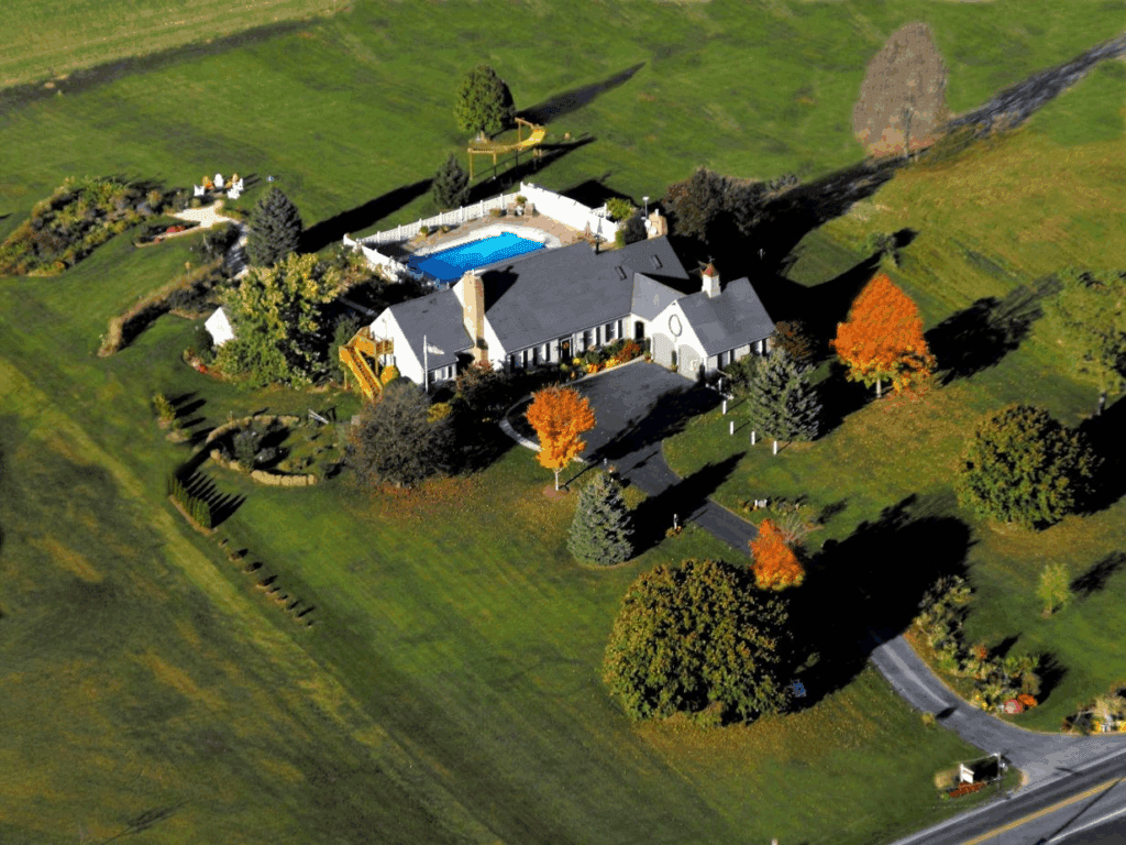 Aerial view of a spacious home with a pool surrounded by colorful trees and landscaped gardens.