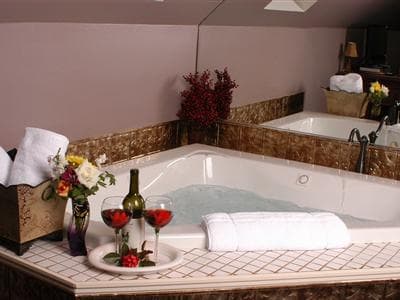 A luxurious bathroom featuring a jacuzzi, fresh flowers, wine, and towels.