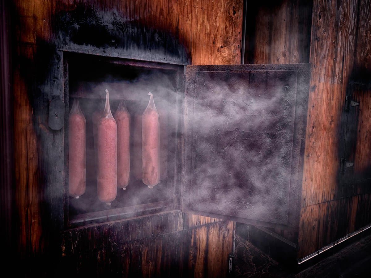 A smoky wooden smoker with hanging sausages inside.