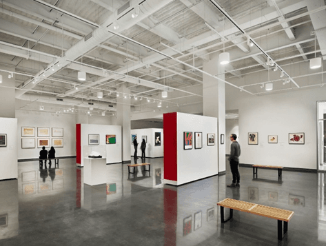 A modern art gallery featuring white walls, colorful artworks, and visitors observing the exhibits.