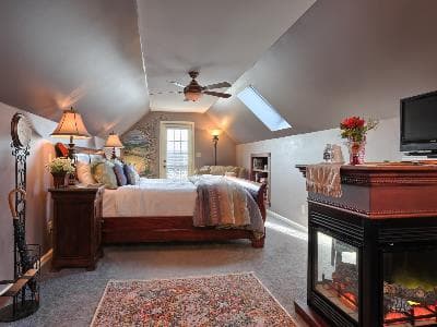 A cozy attic bedroom featuring a large bed, decorative lamps, a fireplace, and a skylight.