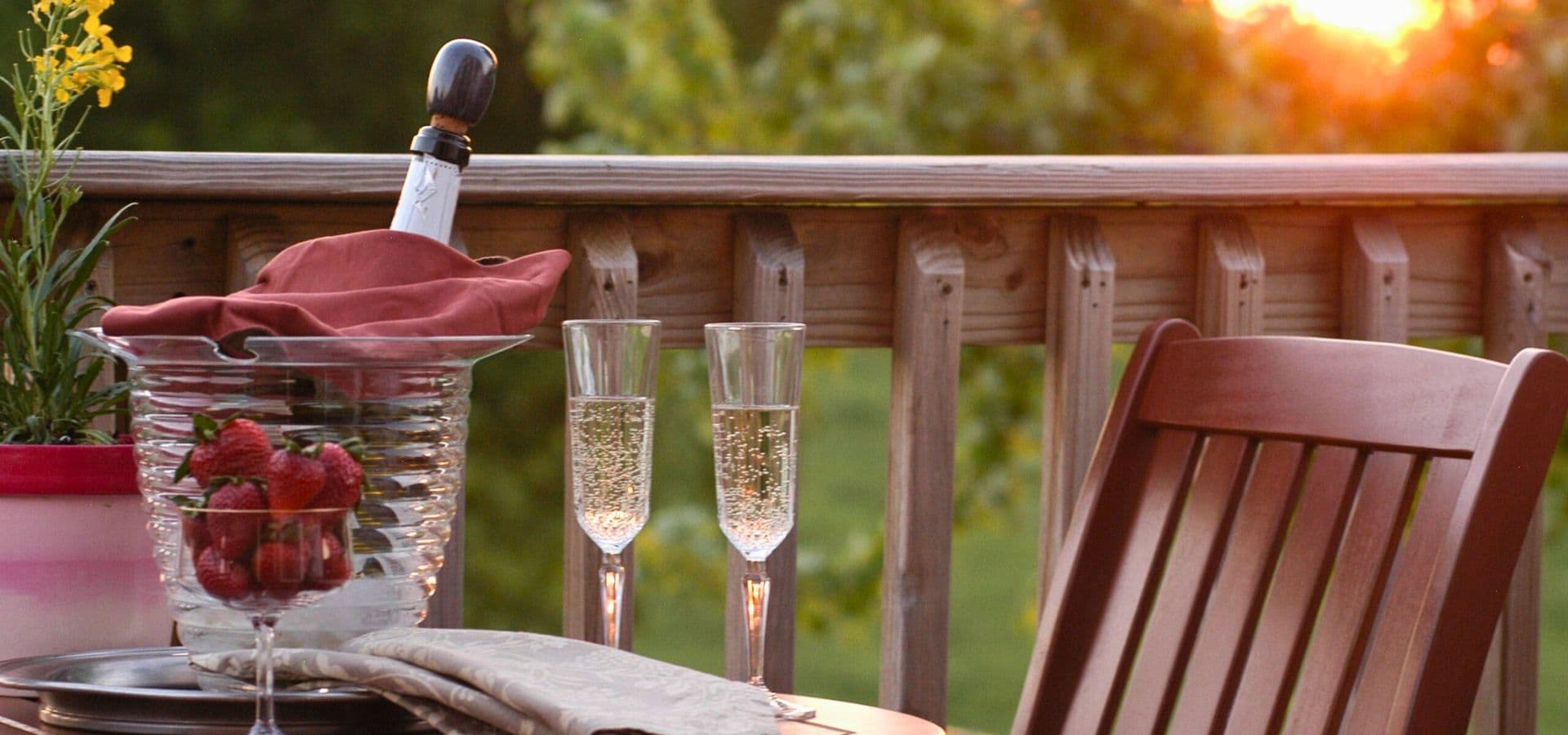A romantic setting with champagne flutes, strawberries, and a sunset backdrop on a wooden deck.