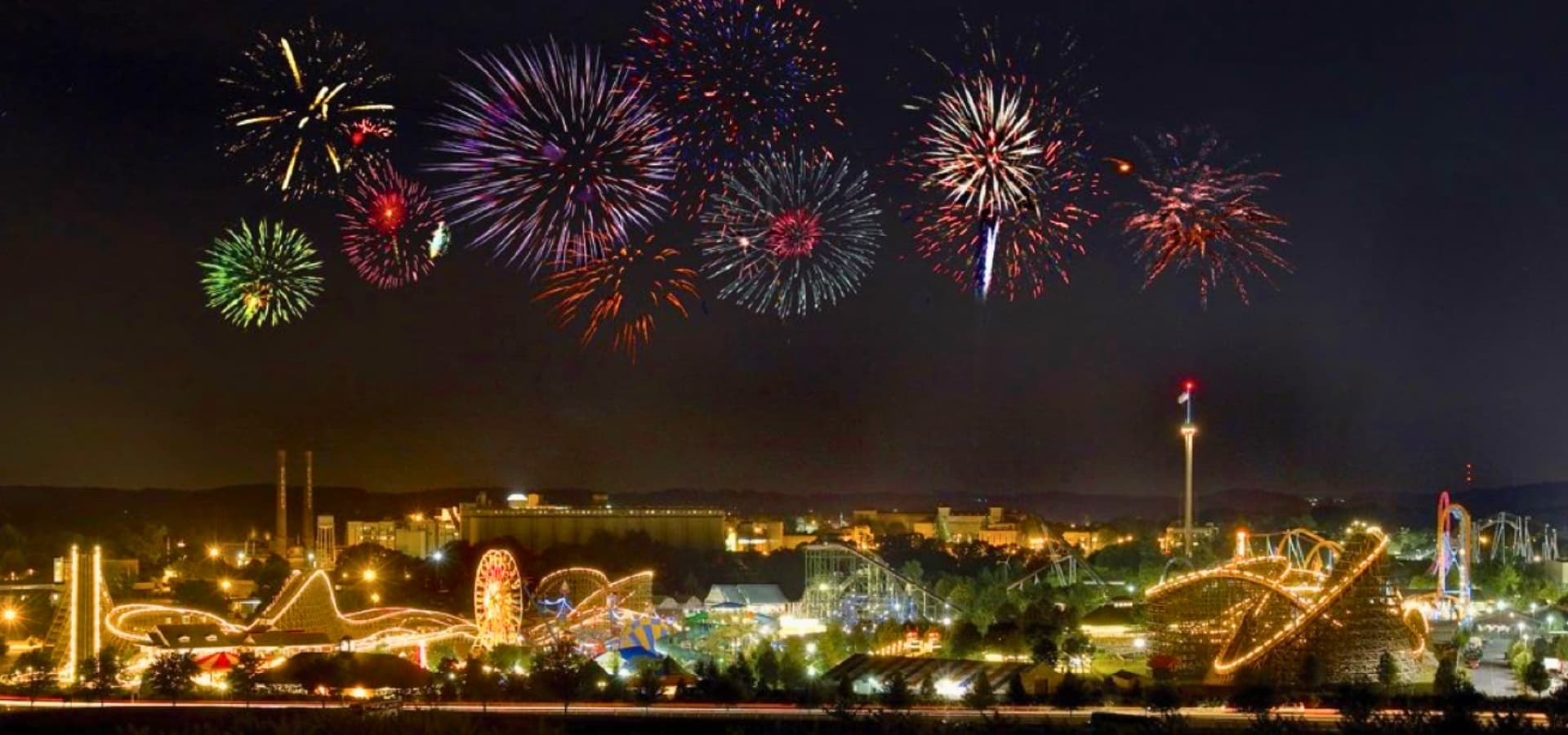 A vibrant fireworks display illuminates an amusement park at night.