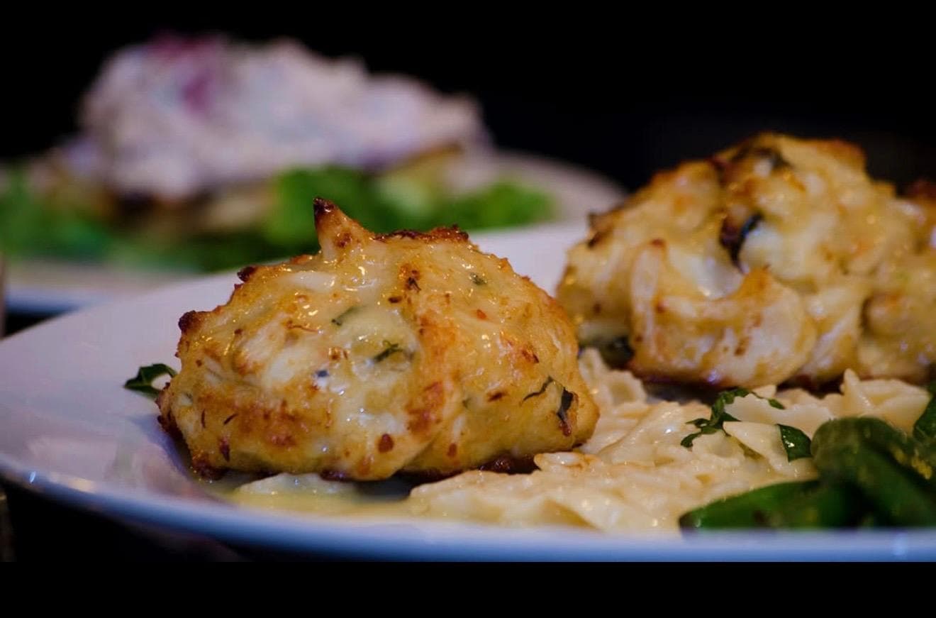 A plate featuring crab cakes alongside creamy pasta and garnished with fresh greens.