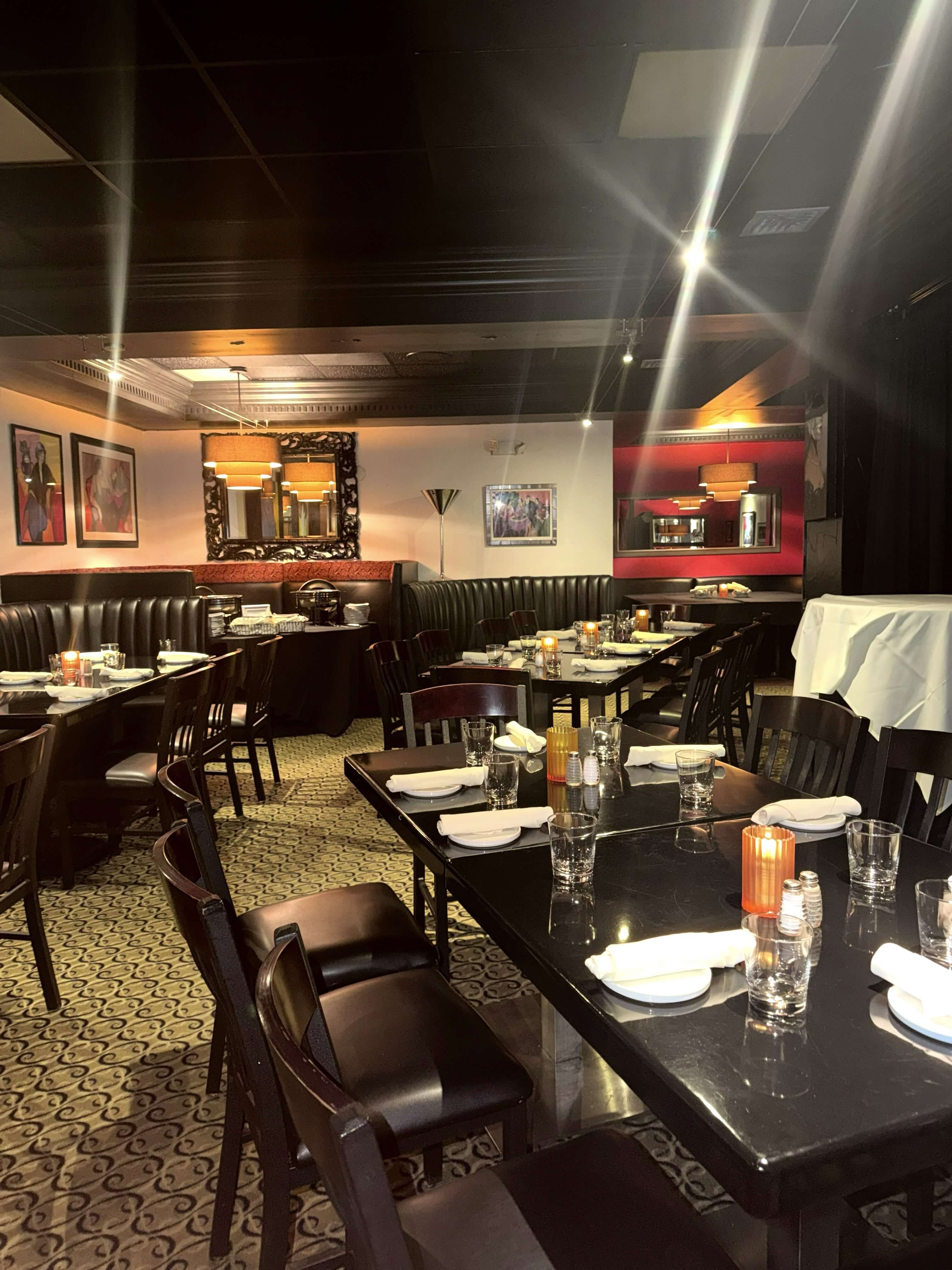 Interior of a dimly lit restaurant featuring black wooden tables, leather booths, and decorative artwork.