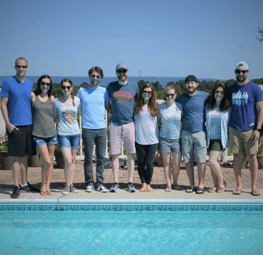 A group of ten friends gathers by a swimming pool on a sunny day.