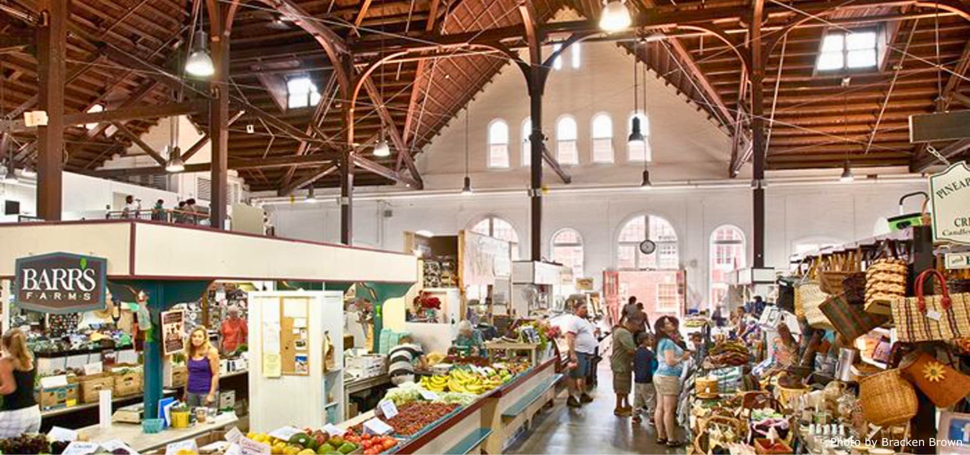 A bustling market interior with wooden beams, various food stalls, and shoppers mingling.