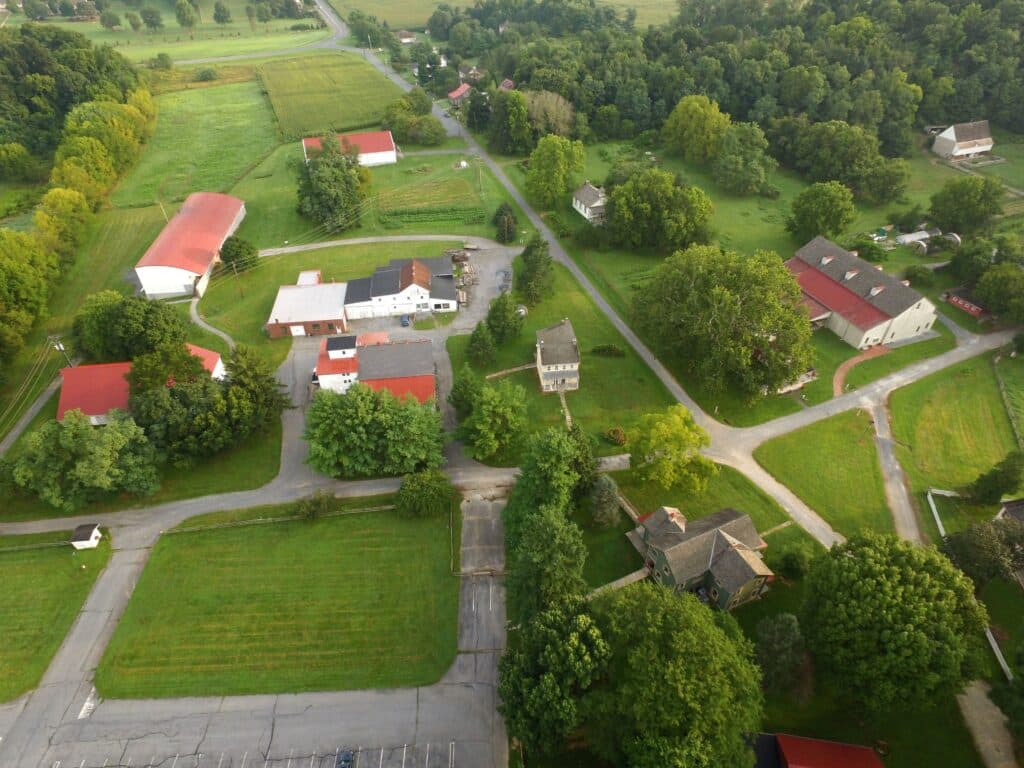 Aerial view of a rural landscape featuring multiple structures, green fields, and winding roads.