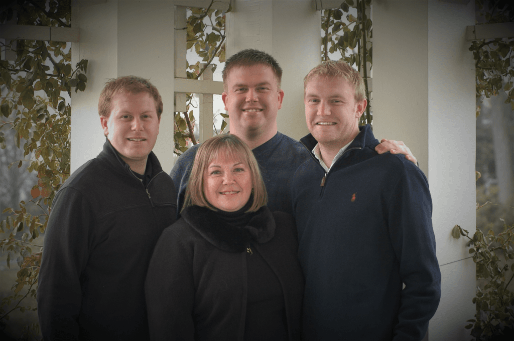 A woman and three men stand together, smiling in a warmly lit outdoor setting.
