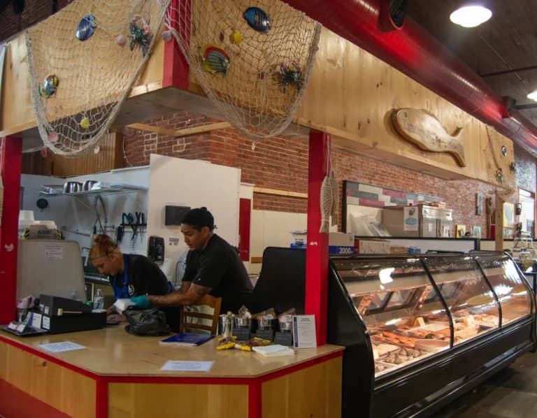 Two employees working at a seafood market counter with a refrigerated display behind them.