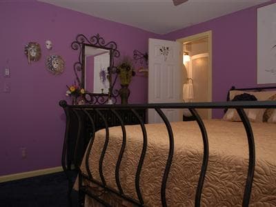 A cozy bedroom featuring a purple wall, ornate mirror, decorative masks, and a wrought-iron bed.
