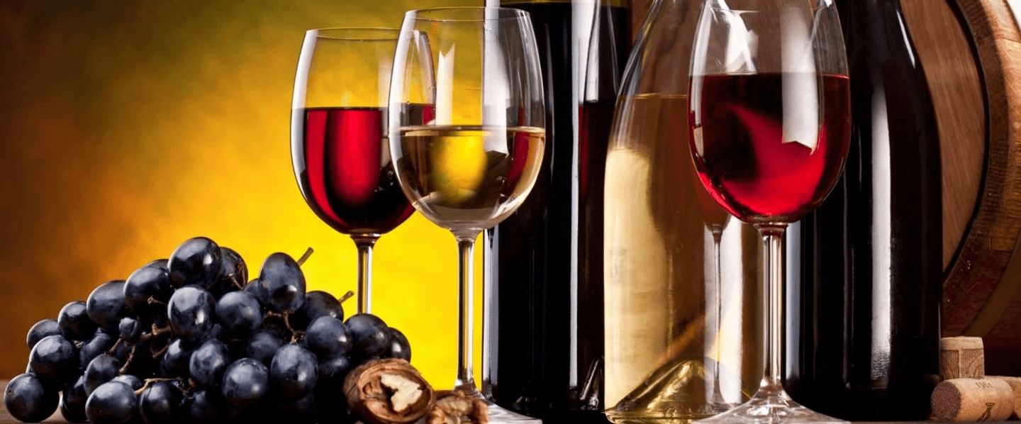 Glasses of red and white wine next to a cluster of grapes and wine bottles.