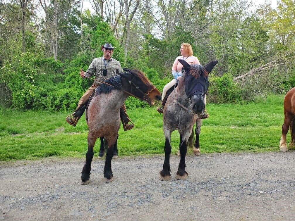 A man and a woman on horseback pose together on a grassy trail.