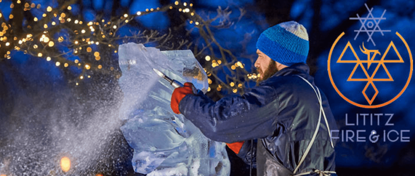 A man in a blue beanie carves an ice sculpture at night, surrounded by twinkling lights.