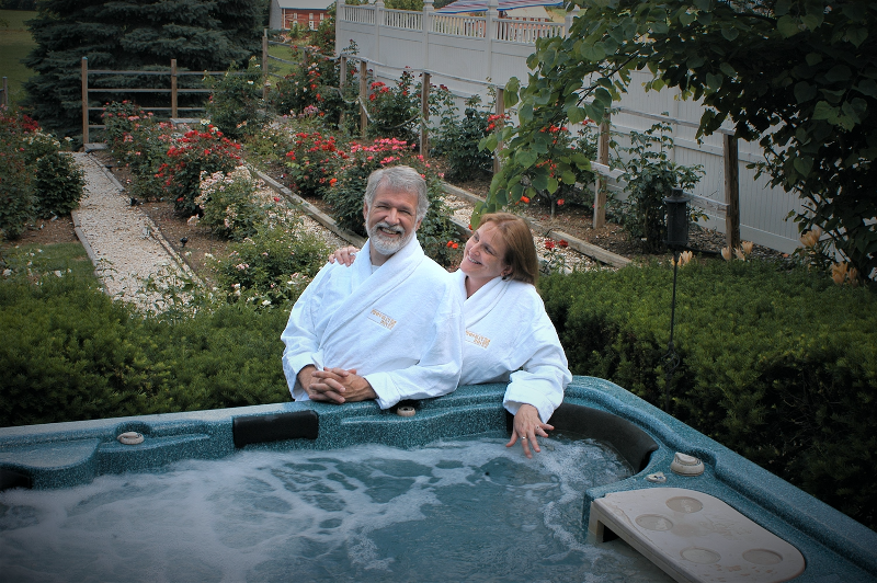 Couple by hot tub in Annville Inn Robes. Part of Rose Garden in background.