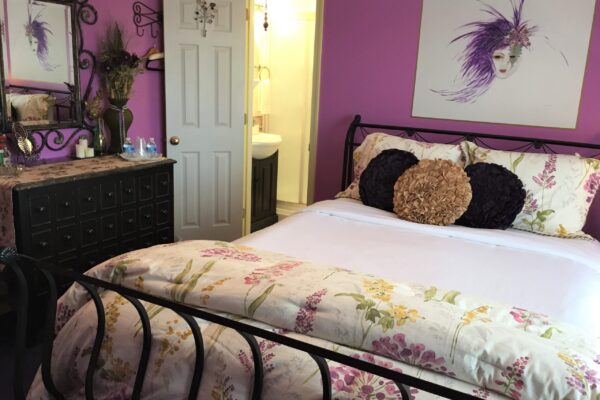 Mardi Gras Bedroom showing Queen bed, hand painted image above bed of Mardi Gras mask in purples, French style marble top dresser.